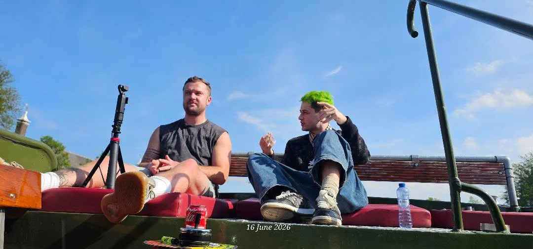 Luc Carlin (LMC): seated outdoors beside a guest and a microphone