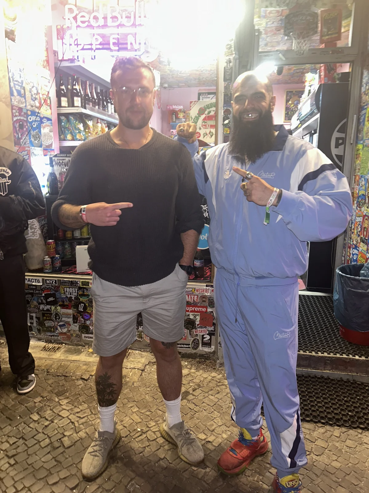 Luc Carlin (LMC) — standing beside a guest in a blue tracksuit indoors