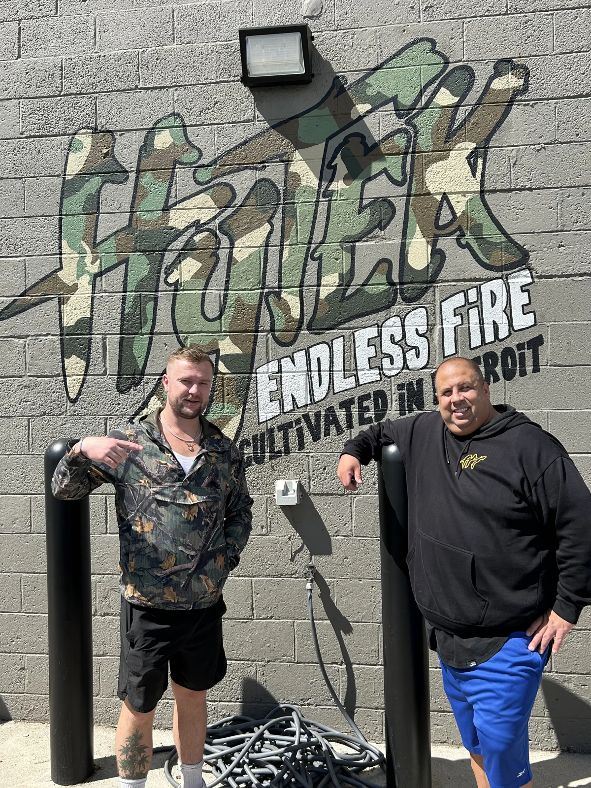 Luc Carlin (LMC) — standing beside a guest in front of the endless fire mural